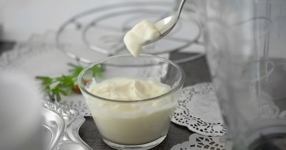 A spoon lifting a scoop of thick plain yogurt from a glass bowl